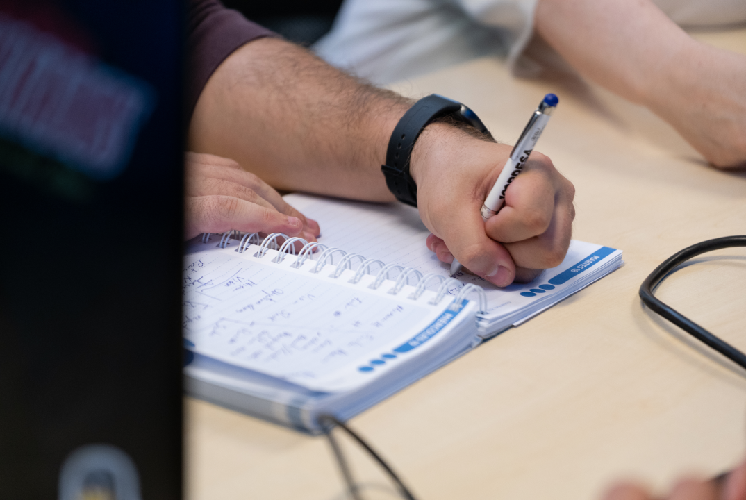 Primer plano de la mano de un hombre escribiendo a boli en un cuaderno aplicando el design thinking para pymes.
